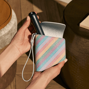Əl Jet Black rəngli Ploom AURA cihazını Ploom İkili Daşıma Qabı Çoxrəngli Naxışlı Kətan-dan çıxarır
