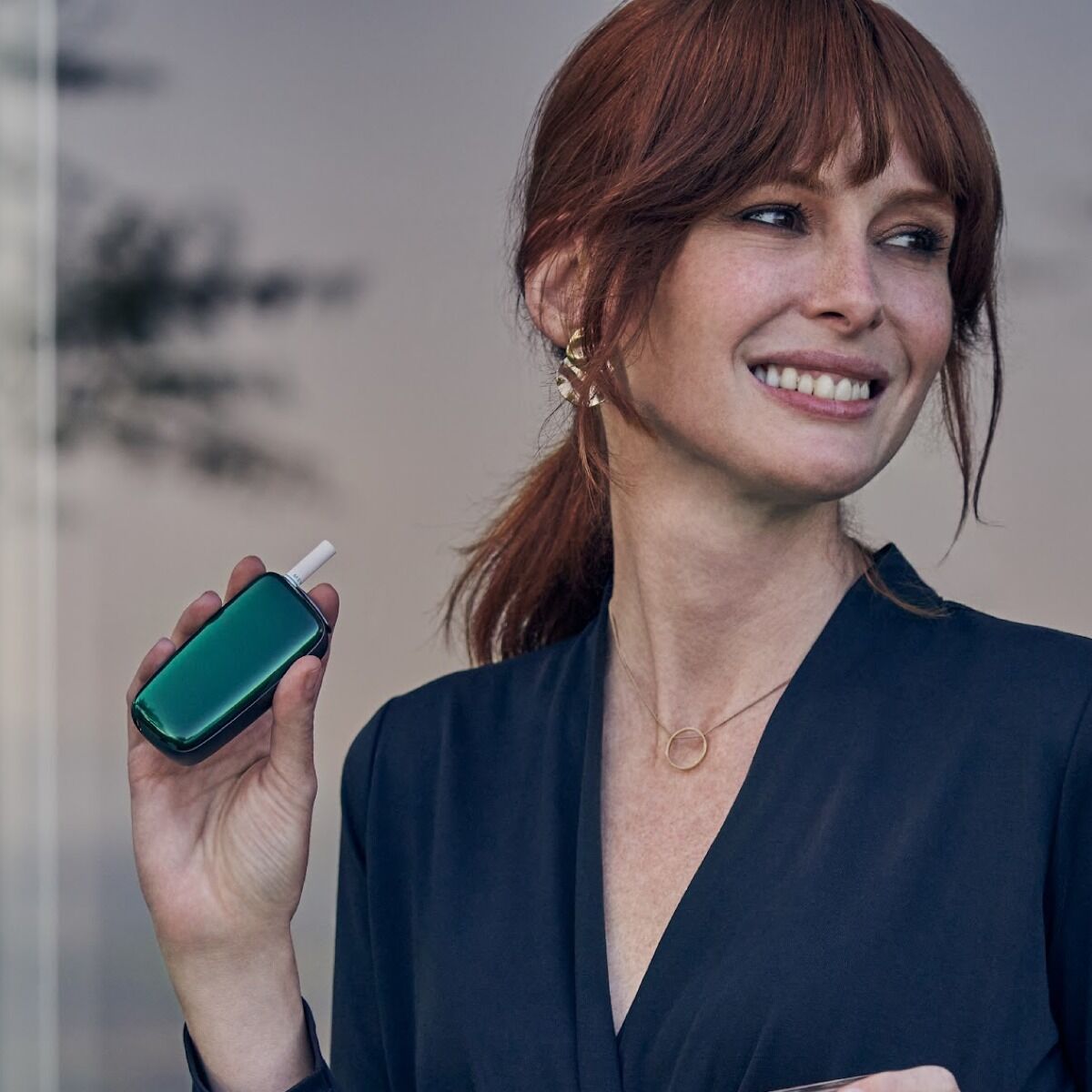 Woman in blue shirt holding Ploom X Advanced with Amazon Green front panel with a tobacco stick, in hand