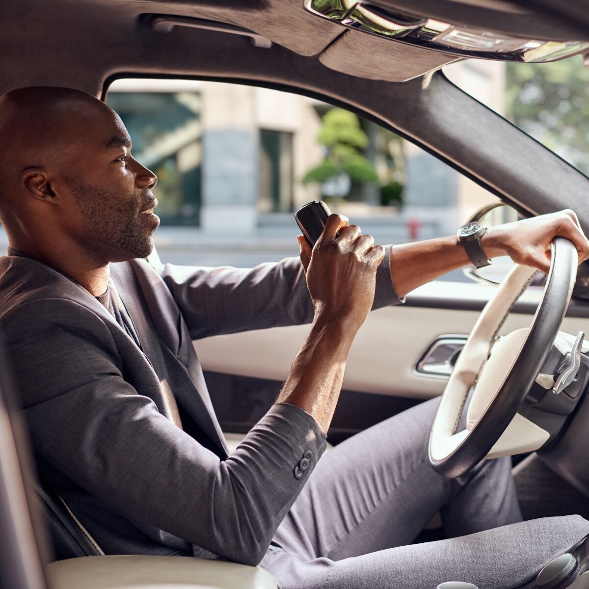 Sükan arxasında olan kişi əlində Ploom X Advanced Black cihazını tutur