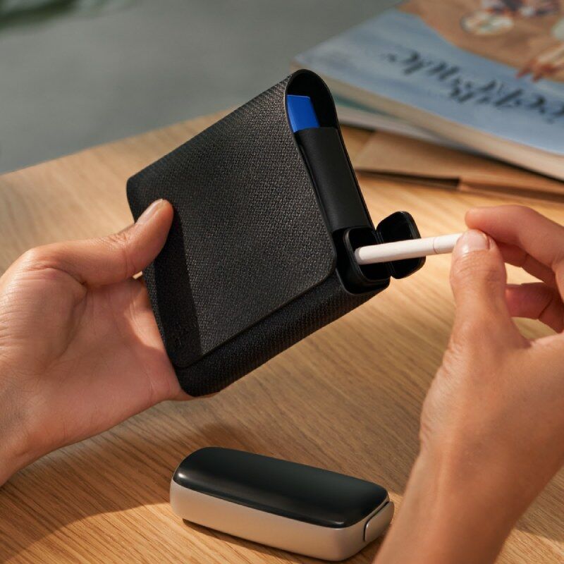 Ploom X Advanced All in One Black shown against a wooden table, someone pulling a stick from the case, next to a Ploom device on the table