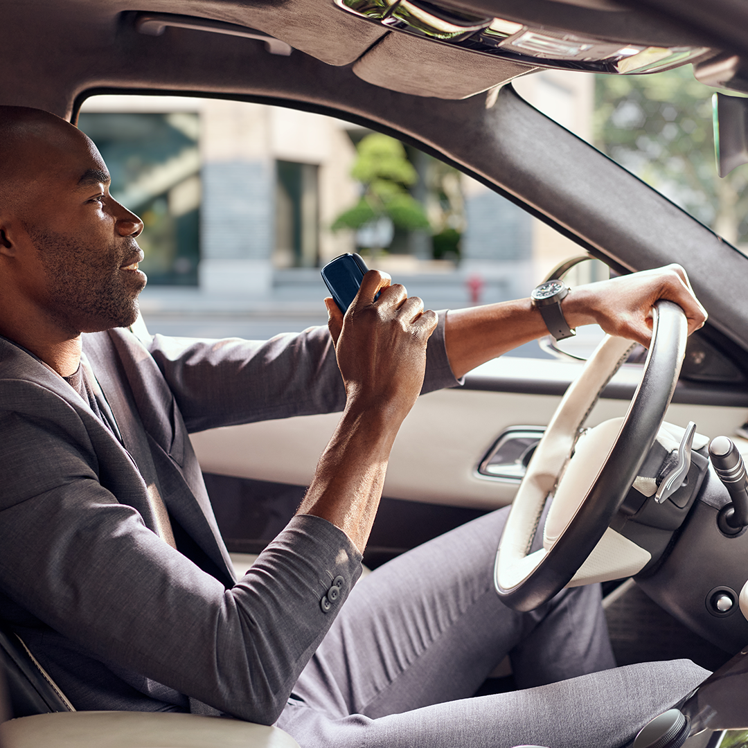 Sükan arxasında olan kişi əlində Ploom X Advanced Navy Blue cihazını tutur
